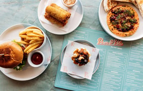 Flat lay of burger, crumbed cheese rolls, loaded brie and romesco spread at Whitestone Cheese Deli & Diner