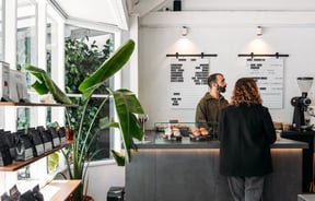 Two people looking in the same direction at a cafe counter.