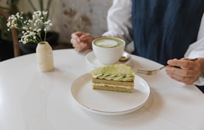 Person sitting at table at Sweet Soul Patisserie with a cup of matcha latte and a beautiful matcha flavoured patisserie
