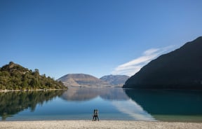 Two people walking along a lake on a sunny day.