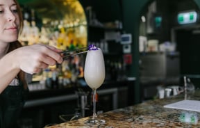 Bartender adding purple pansy as a garnish on top of a cocktail