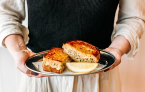 A person holding a plate of grilled cheese and tuna toasted sandwich.