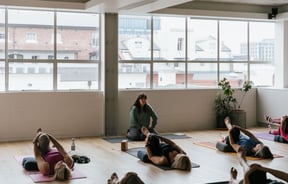 A yoga teacher taking a class of students lying on their backs.