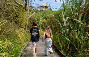 Two children running on the boardwalk in and amongst native bush.