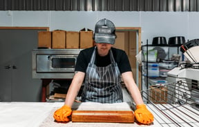 Baker rolling out dough in the kitchen at The Baked Dane.