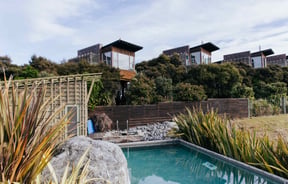 Wooden apartments set behind a swimming pool on a sunny day.