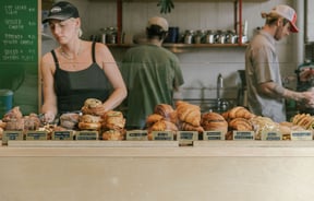 Three staff members behind the counter at Grizzly, with a cabinet filled with croissants, morning buns and filled bagels