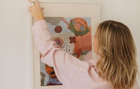Woman hanging art print on the wall by Mathilde Langevin.