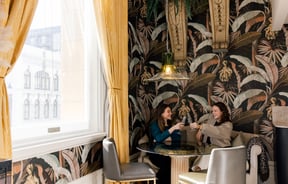 Two women toasting their wine glasses sitting at a table.