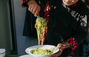 A chef serving a plate of spinach pasta on a plate in the sunlight.