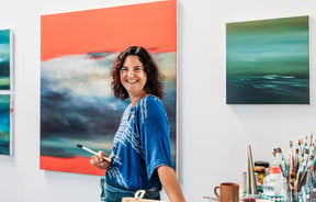 A woman holding a paint brush and smiling to camera.