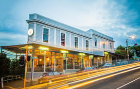 A photo of a blue building with cars whizzing by out front at dusk.