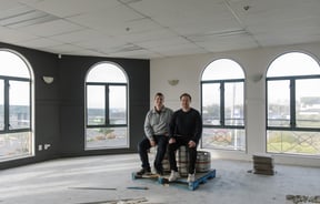 Two men sitting in an empty room smiling to camera.
