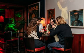 People sitting around in a dimly lit room drinking.