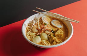 A plate of laksa on an orange table.