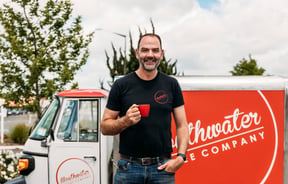 A man holding a red cup of coffee outside a coffee cart.