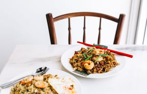 A bowl of noodles and a bowl of fried rice against a white background.