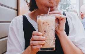 Close up of a woman sipping on an iced coffee in a big glass.