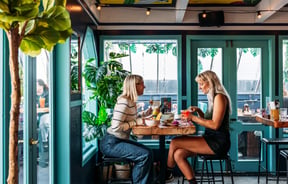 Two women dining at a high table inside a green painted room.