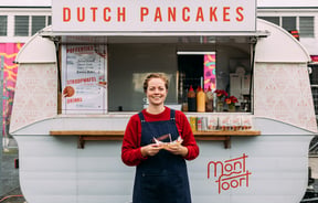 A woman holding Dutch pancakes in front of a white caravan.