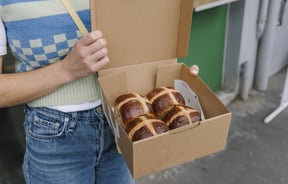 Person holding box of four Hot Cross Buns outside Grizzly in Christchurch