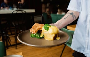 Someone holding a plate of eggs hollandaise with smoked salmon on the side