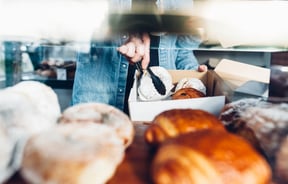 Person in denim jacket using tongs to put donuts and croissants into a take away container.