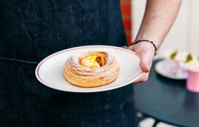 A hand holding a pastry on a plate.