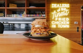 A Chicken burger on a black plate sitting on a wooden bench.
