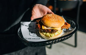 Someone holding a fried chicken burger with a sesame seed bun.