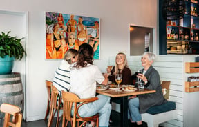 A group of women cheers their drinks over a table of food.