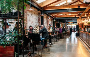 People sitting at high tops in a brick brewery building.