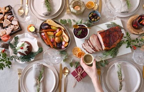 A hand holding a glass of champagne over a Christmas table setting.