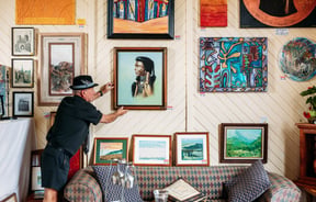 A man hanging art work on a wall inside a gallery.