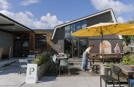 Large yellow outdoor umbrellas in front of the asymmetrical, black frontage of Dune Cafe in New Brighton.