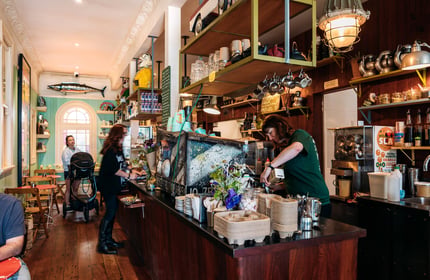 Barista making coffee behind cafe counter and cabinet