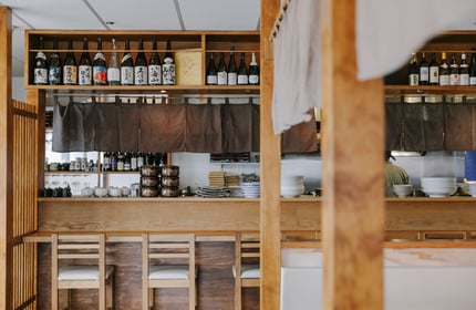 Looking over the counter into the kitchen where the chef is.