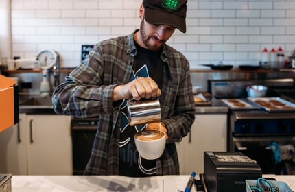 Barista pouring milk into freshly made coffee at cafe