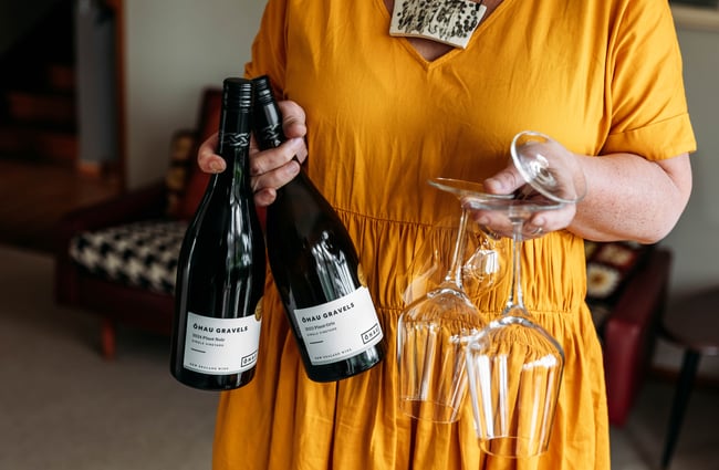 Manager holding two bottles of wine and some glasses at Ōhau Wines.