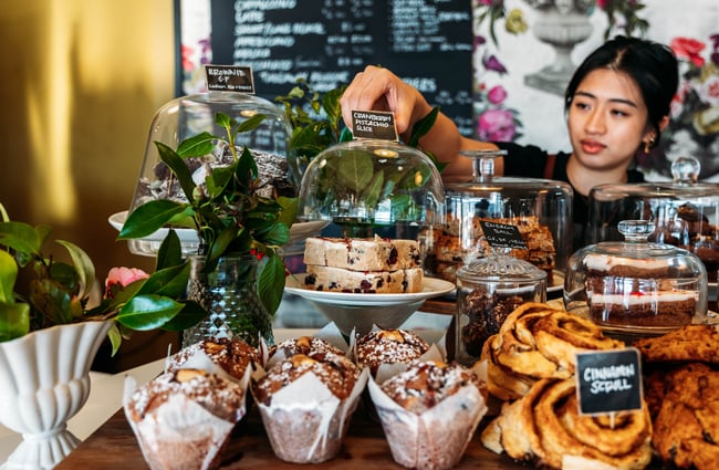 A staff member reaching for a sweet treat on the counter at The colourful interior of 103 The Store Roxburgh Central Otago.