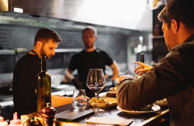 Wine bottle and glass on the bar with the open kitchen in the background at 5th Street restaurant Christchurch.