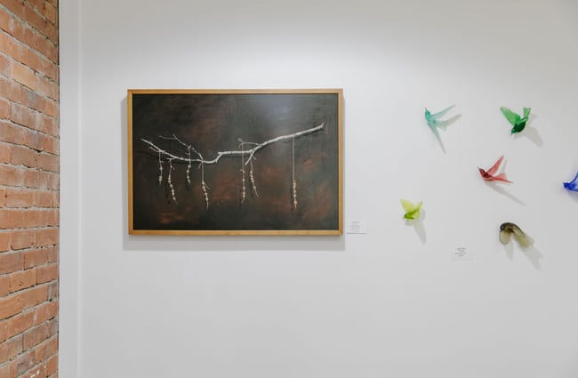 Colourful glass birds on a wall next to a dark painting at 77 Art + Living in Fairlie.