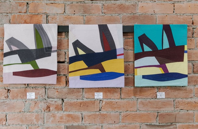 Three colourful paintings lined up on a brick wall at 77 Art + Living in Fairlie.