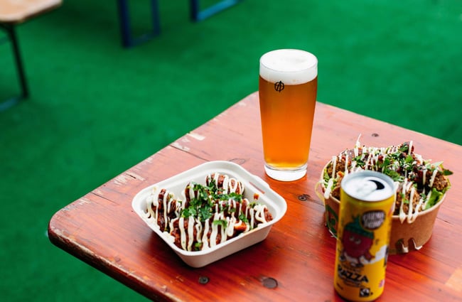 Two take away containers of food on a wooden table with a fresh brewed drink.