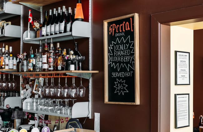 A specials chalkboard on the wall beside the wine, spirits and wine glasses shelving.