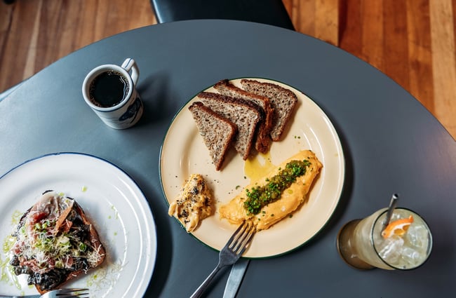 Birds eye view of a mushrooms on toast dish, scrambled eggs and toast dish, a mug of black coffee and a cold drink in a glass.