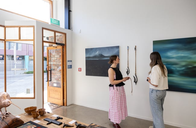 Gallery owner and a customer stand in front of the wall with two large artworks at Ashe.