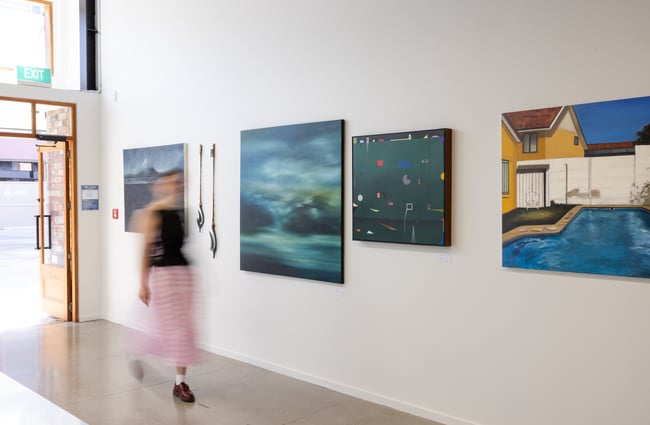 Gallery owner walking through the exhibition space with artworks on the wall at Ashe.