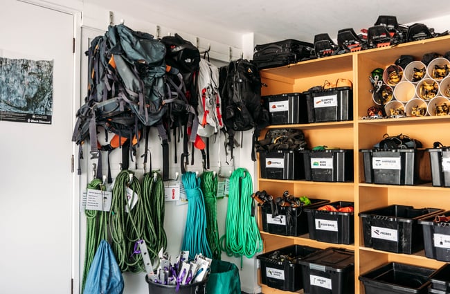 Backpacks hanging on the wall beside containers of equipment at Aspiring Guides.