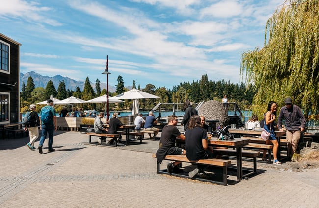 People dining outside by a lake on a sunny day.